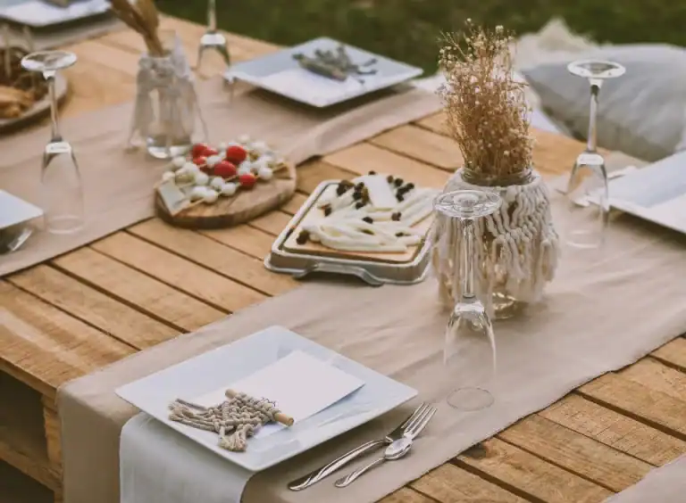 HOMCOM Holztisch mit weißen Tellern, Besteck, Weingläsern, Käseplatten und Trockenblumenvasen.