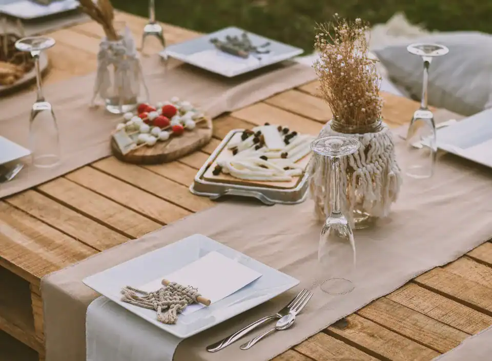 HOMCOM Holztisch mit weißen Tellern, Besteck, Weingläsern, Käseplatten und Trockenblumenvasen.
