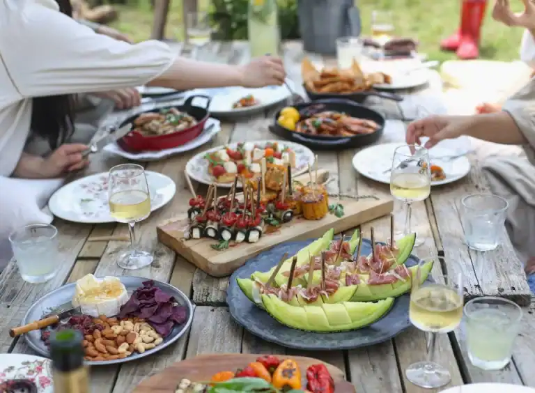 Eine Gruppe genießt den Komfort von HOMCOM, während sie sich an einem Holztisch im Freien Vorspeisen, Obst und Wein teilt.