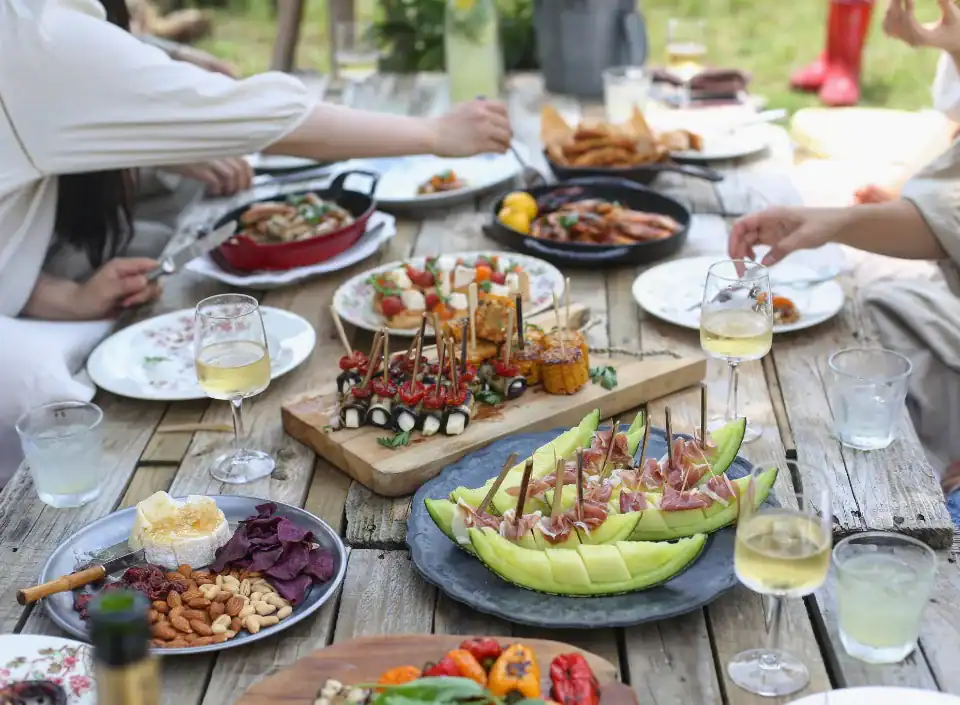 Eine Gruppe genießt den Komfort von HOMCOM, während sie sich an einem Holztisch im Freien Vorspeisen, Obst und Wein teilt.