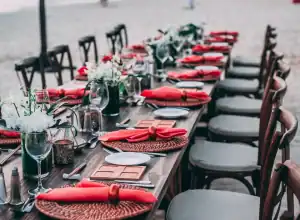Ein langer HOMCOM-Esstisch im Freien, gedeckt mit roten Servietten, Gläsern und floralen Tafelaufsätzen auf gewebten Tischsets.