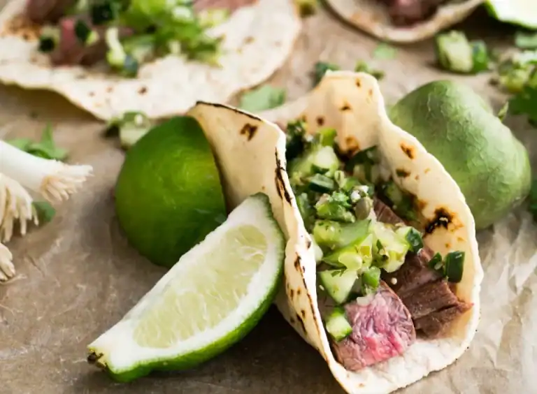 Ein HOMCOM-Steak-Taco mit frischer Salsa und zwei Limettenspalten, serviert auf Pergamentpapier.